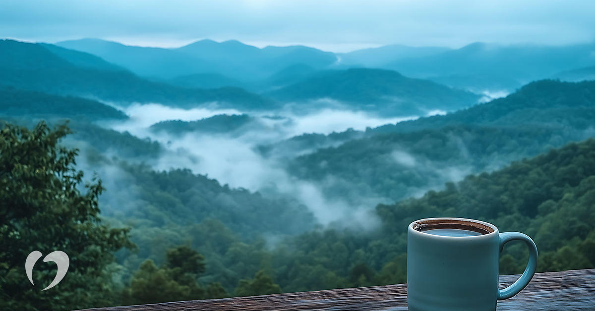coffee cup on the ledge of a balcony overlooking a scenic view of fog-covered mountains