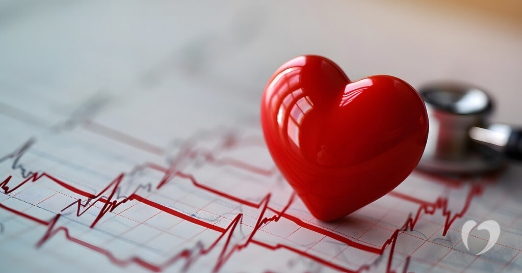 A red heart model sits on an electrocardiogram (ECG) printout, with a stethoscope in the background.